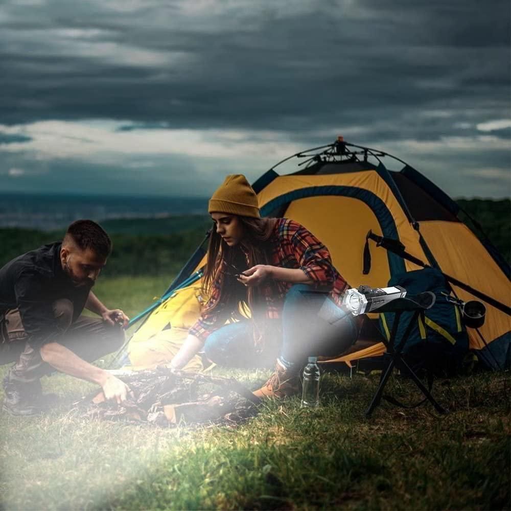 Couple camping using a portable rechargeable LED flashlight to light the campfire near a yellow and blue tent